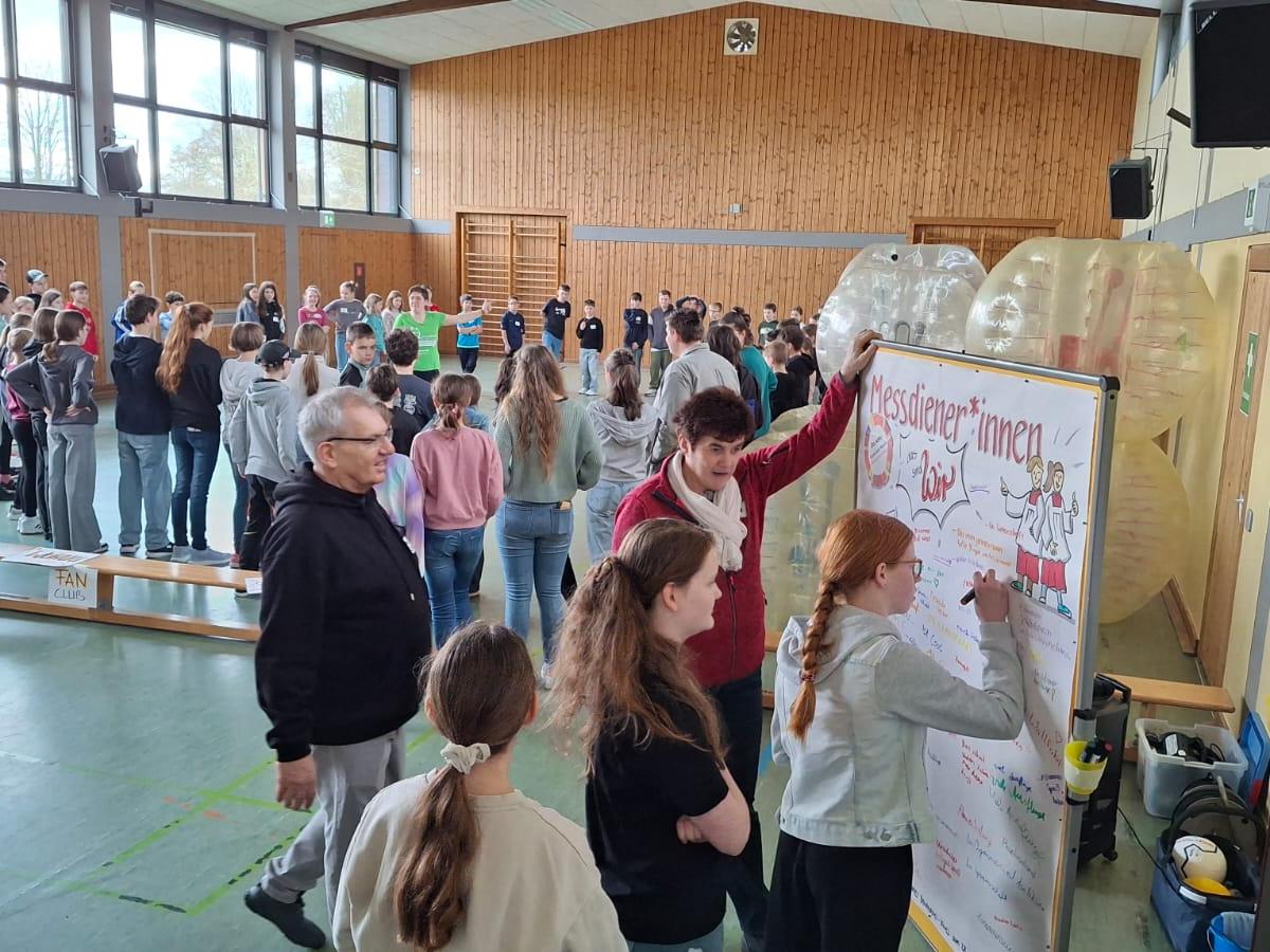Man sieht Kinder und Jugendliche in einem großen Raum, die in verschiendenen Workshops eingeteilt sind.